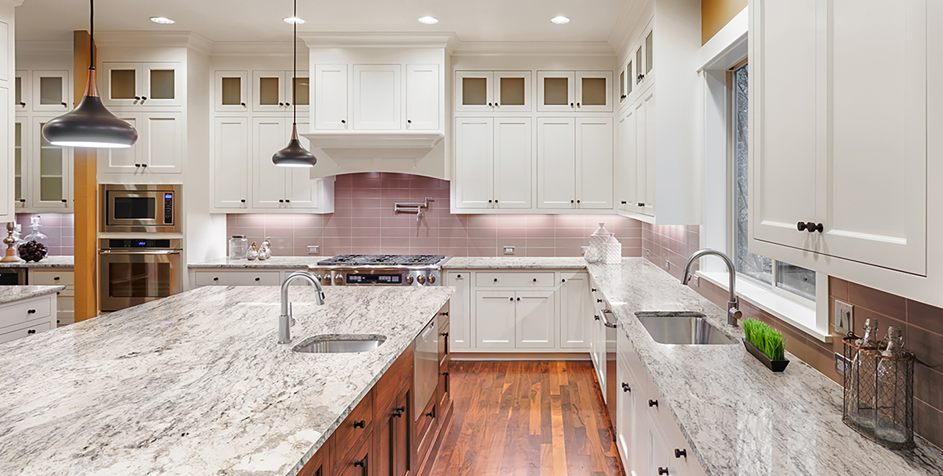Large kitchen interior with hardwood floors, two sinks, pendant lights, and wrap around cabinets